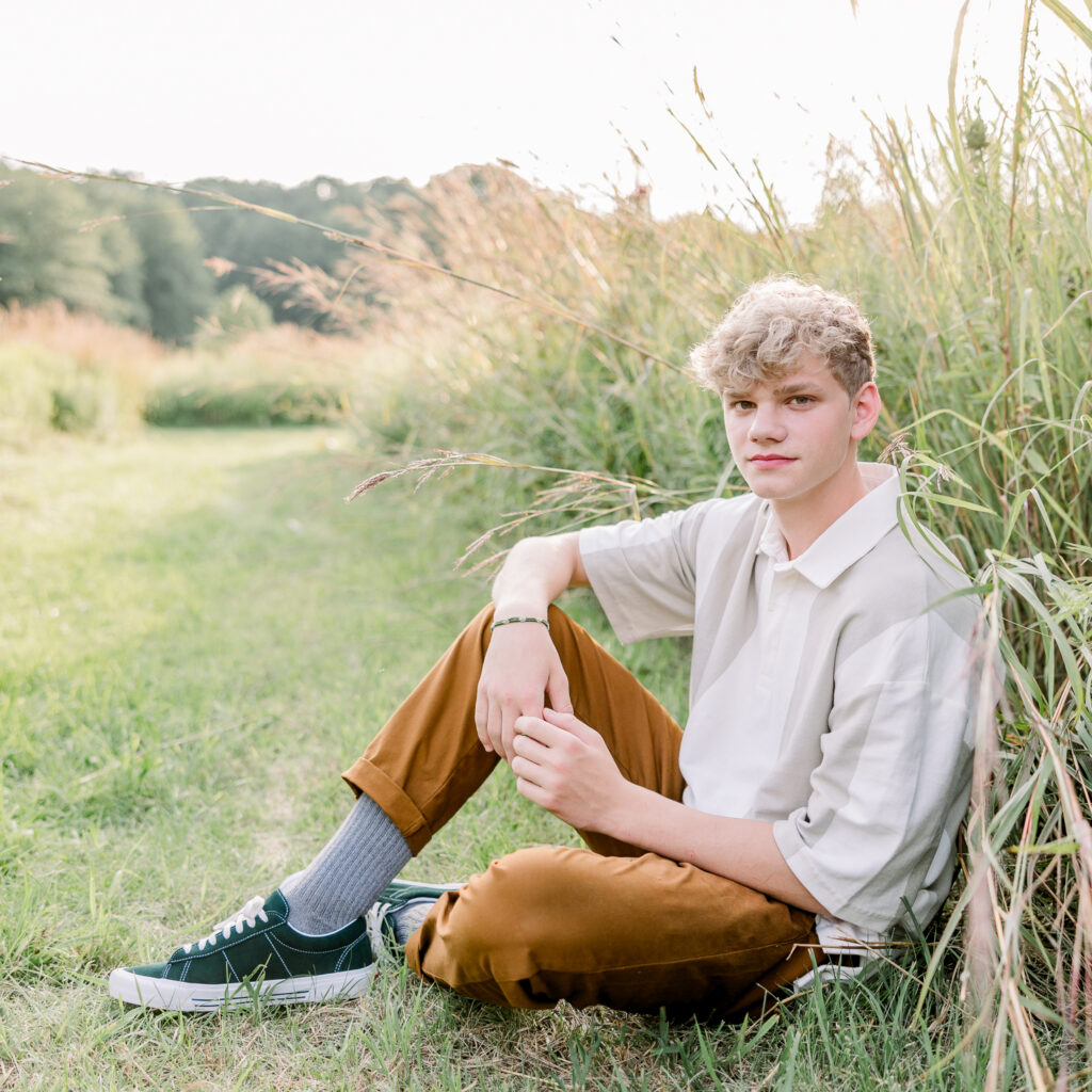 Boy sitting next to tall grass with arm resting on leg at a state park