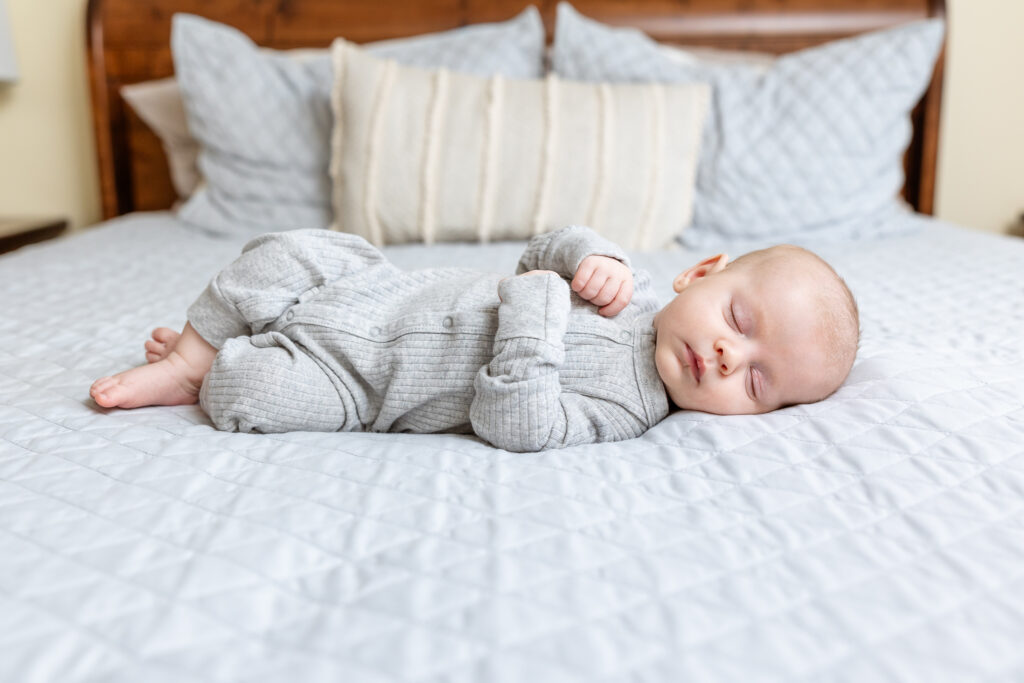 Baby wearing gray jumper sleeping on bed 