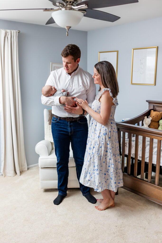 Mom wearing white and blue dress and Dad wearing white shirt. Mom, Dad, and Newborn in nursery 