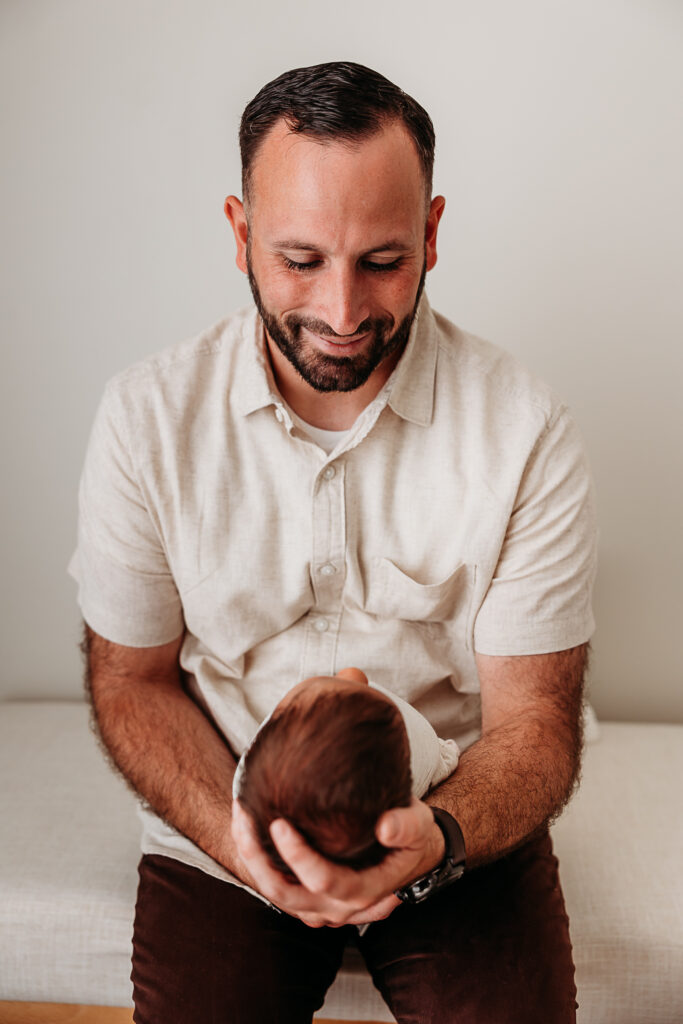 Dad holding and smiling newborn baby. Example of neutral toned shirt for partner from fresh 48 photography guide