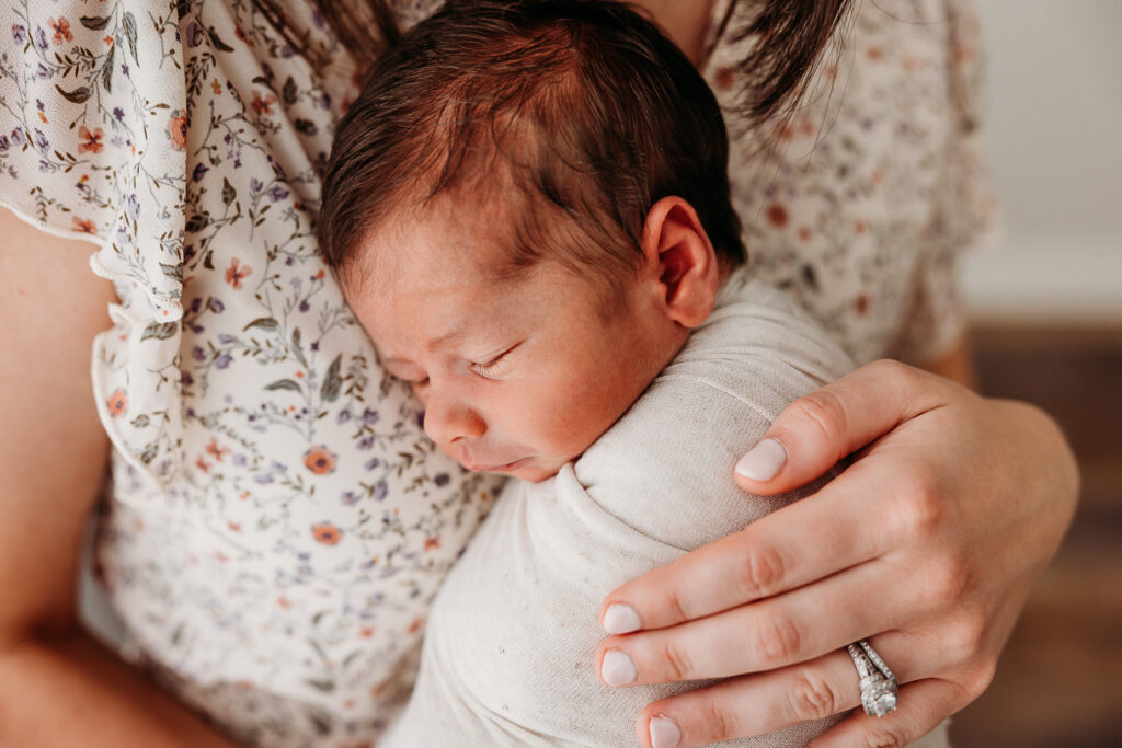 Mom holding newborn to give an example of how to hold a baby to chest with light from window for fresh 48 photography
