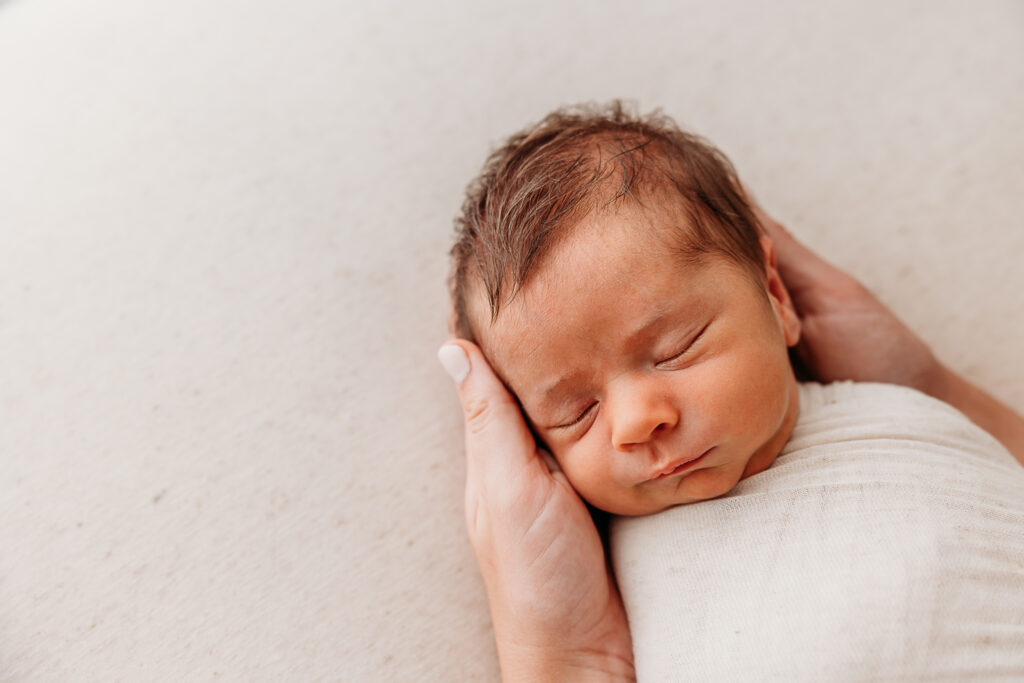Moms hand behind baby's neck in a close up image of newborn baby boy, example image for close up of baby's face from fresh 48 photography guide