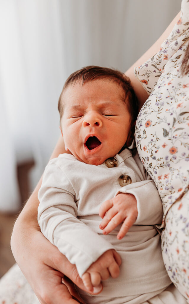 Newborn baby yawning in moms arms in example outfit from fresh 48 photography guide
