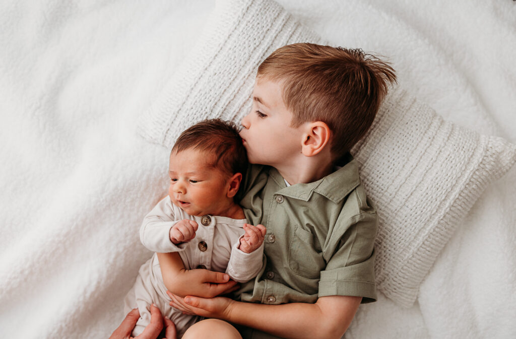 Big brother kissing the top of newborn brother baby's head. Example of clean and non distracting background from fresh 48 photography guide 